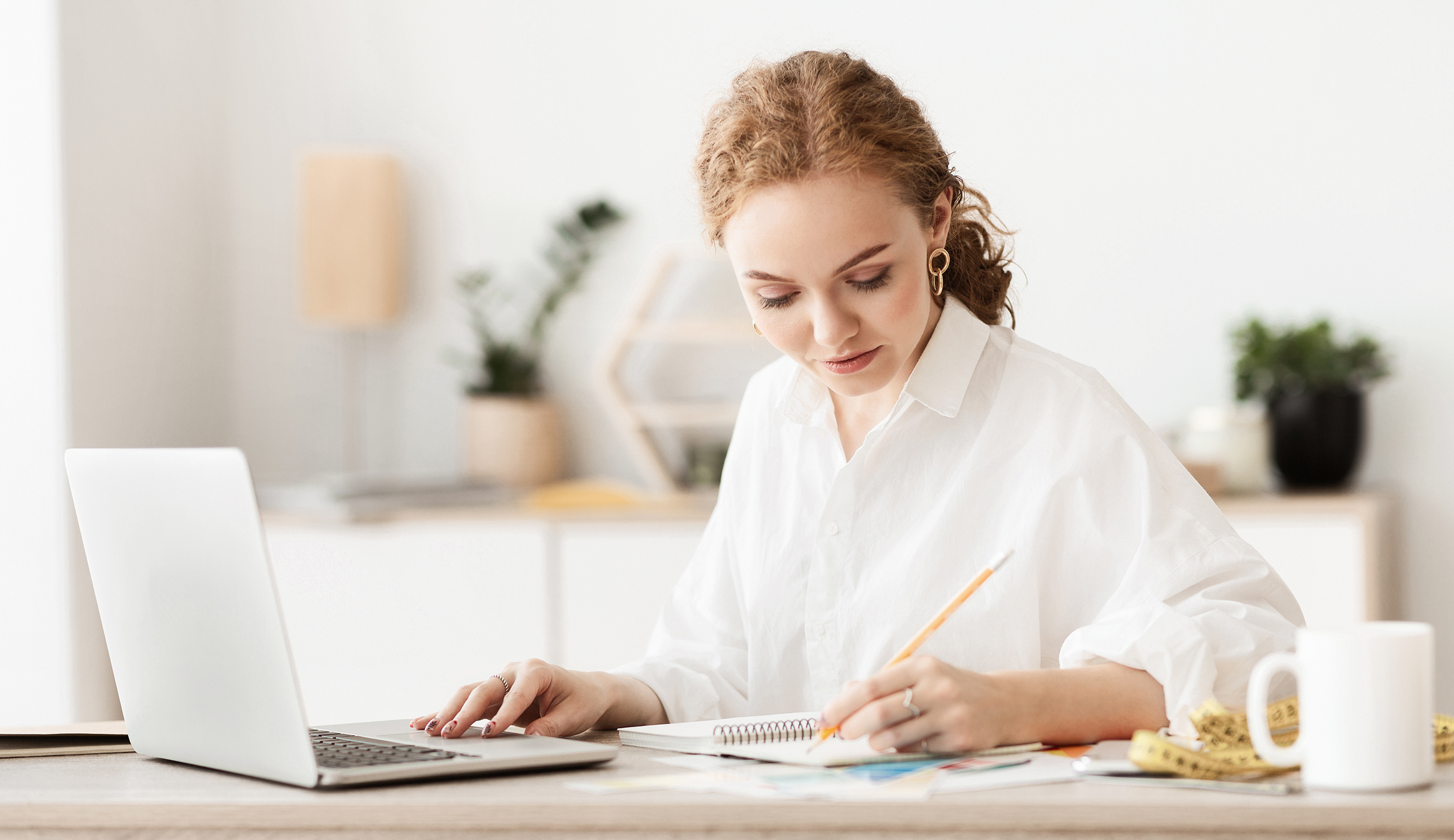 woman writing whilst working on laptop